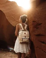 Mochila Cabaia modelo Adventurer Alger, de diseño estructurado en color blanco con detalles en tono dorado metalizado en la base y las asas superiores. Cuenta con un bolsillo frontal con cierre, parche circular con logo de la marca y tiradores de cuero sintético.