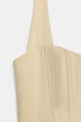 Top estilo corsé color beige, con escote recto, cuello halter y bajo asimétrico. Presenta costuras estructuradas frontales.