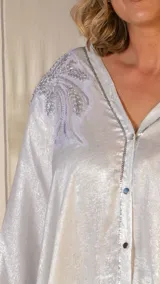 Levita larga de color plateado con diseño holgado tipo kaftan. Presenta cierre frontal con botones y detalles de bordado con pedrería en los hombros. Las mangas son amplias y el largo llega hasta los pies.