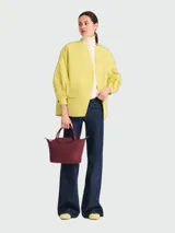 Cartera de mano modelo Le Pliage One de Longchamp, tamaño pequeño, en color bordó. Presenta un diseño icónico con solapa de cuero, cierre de botón a presión y asas cortas. Fabricada en material resistente con acabado mate.