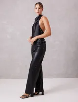 Pantalón de cuero sintético negro, de corte recto y tiro alto. Presenta cintura con hebillas laterales regulables y cierre frontal.