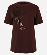 Remera de algodón de corte recto, con cuello redondo y mangas cortas. Presenta un diseño decorativo de lentejuelas bordadas en la parte frontal.