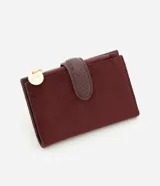 Billetera tipo sobre de Satinato, confeccionada en material sintético efecto gamuza color bordó. Presenta un cierre principal con tirador metálico circular grabado y una solapa central con textura tipo reptil.