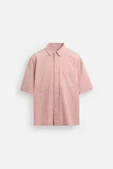 Camisa de corte relajado confeccionada en algodón, con estampado de cuadros pequeños en tonos rosados. Presenta cuello solapa, manga corta y bolsillo plastrón en el pecho con cierre frontal de botones.
