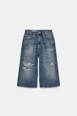Bermuda tipo jorts de tiro medio confeccionada en denim azul con efecto lavado. Presenta diseño de cinco bolsillos, roturas decorativas y ruedo desflecado.