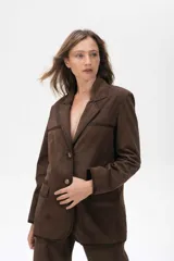 Blazer de ante color marrón con silueta oversize, cierre frontal con botones, bolsillos con solapa y tajo trasero. Presenta detalles de costuras con terminaciones pintadas a mano.