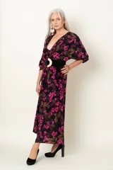 Vestido midi de seda natural con estampado floral en tonos fucsia sobre base negra. Presenta un diseño drapeado con escote en V cruzado, mangas largas abullonadas y una abertura frontal en la falda.
