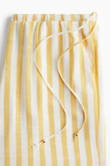 Pantalón de corte holgado con piernas amplias y bolsillos al bies. Modelo de tiro bajo con elástico revestido y cordones para ajustar enlazados a los lados, decorados con cuentas en los extremos.