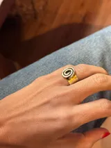 Anillo de diseño artesanal con motivo de espiral en la parte superior, elaborado en bronce con acabado bicolor.