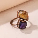 Anillo abierto y ajustable con diseño orgánico en tono cobre, engastado con dos piedras naturales en bruto: una amatista de color violeta y un topacio o fluorita de color amarillo.