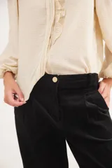 Pantalón recto de tiro medio confeccionado en pana con lycra. Presenta pinzas frontales, bolsillos laterales y traseros, y cierre con botón dorado. El diseño destaca por el detalle de paño espigado en el interior del ruedo, visible al doblarlo, y un pin bordado decorativo en el bolsillo delantero.