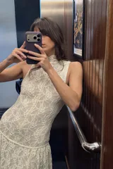 Vestido largo de encaje color blanco roto, con cuello alto, sin mangas y corte evasé. Incluye forro interior y cierre en la espalda.