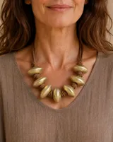 Collar de cuero marrón con abalorios grandes de metal dorado envejecido con forma de almendra distribuidos a lo largo de la pieza.