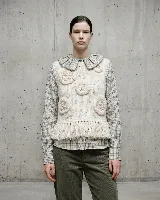 Chaleco de lana merino color crudo, con diseño artesanal que presenta apliques florales en relieve y terminación de flecos en el ruedo.