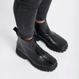 Bota corta de cuero vacuno color negro, con suela de goma tipo track y punta cuadrada. Presenta un detalle central de cuero con textura de reptil y cierre lateral interno.