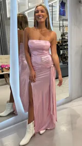 Vestido largo strapless de tejido metalizado en color rosado, con diseño ajustado, tajo lateral pronunciado y detalle fruncido con argolla dorada en la cadera.