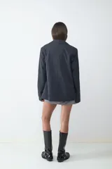 Blazer negro de corte recto y diseño oversize, con cuello de solapa, cierre frontal de dos botones y bolsillos con solapa en los laterales. Interior forrado.