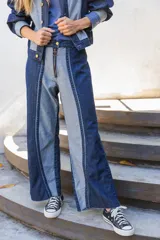 Jean de corte recto confeccionado en denim de algodón, con diseño bicolor que combina paneles en azul oscuro y azul claro. Presenta cierre frontal con cremallera y diseño de costuras verticales marcadas.
