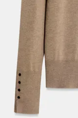 Jersey de punto liso con cuello redondo y manga larga. Presenta detalle de botones decorativos en los puños.