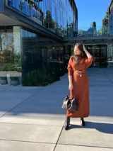 Vestido midi de tricot color caramelo, con cuello alto, mangas largas y cinturón marrón.