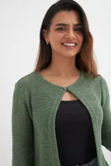 Cardigan verde esmeralda de tejido de punto calado, con mangas 3/4 y corte evasé. Presenta cuello redondo con abertura en forma de gota y cierre con un único botón.