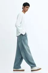 Jeans de cinco bolsillos en denim de algodón rígido, color celeste claro con efecto desgastado/lavado. Modelo de corte super holgado (baggy) desde la cadera hasta el tobillo, con piernas redondeadas extraamplias y tiro bajo.