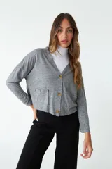 Cardigan de tejido de punto color gris melange, con escote en V, cierre frontal con botones y bolsillos tipo cartera. Presenta un diseño de corte recto y mangas largas.