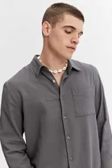Camisa rústica de manga larga color gris oscuro, con cuello clásico, cierre frontal con botones y un bolsillo aplicado en el pecho.