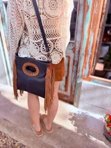 Cartera bandolera negra de cuero con forro interno de tela, detalle de flecos de cuero marrón en la parte inferior y asa larga regulable.