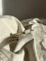 Pulsera rígida dorada con una perla rectangular blanca en el centro.