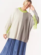 Buzo tejido oversized con bloques de color blanco y gris, cuello redondo en verde neón, tajos laterales y flecos verdes en las mangas.