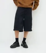 Pantalón cargo de corte mega baggy, color negro, confeccionado en sarga de algodón. Presenta múltiples bolsillos funcionales y un diseño versátil que permite transformar la prenda en bermuda mediante un sistema de ajuste en las piernas.