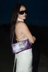 Mini cartera de cuero color violeta metalizado, con diseño rectangular, cierre superior y correa corta para llevar al hombro.