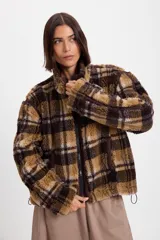 Campera de corderito sintético con diseño a cuadros en tonos marrones y negros. Presenta cuello alto, cierre frontal completo y detalles de paneles en color marrón liso. El diseño es de silueta holgada, largo tipo crop y cuenta con un cordón elástico ajustable en el ruedo.