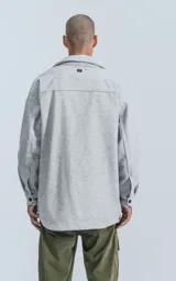 Chaqueta tipo sobrecamisa de paño color gris melange, con cuello clásico, cierre frontal con botones a presión, dos bolsillos superiores con solapa y dos bolsillos laterales. Presenta un diseño de corte recto y holgado.