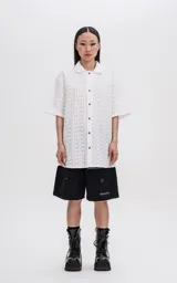 Camisa de manga corta en color off-white, con cuello clásico y cierre frontal de botones. Presenta un diseño con textura de rayas verticales y motivos circulares.