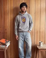 Canguro con capucha de corte regular, color gris con efecto stone wash. Presenta un estampado frontal de una máscara de luchador en tonos azul y naranja, con el logo de la marca debajo. Incluye bolsillo tipo canguro y puños acanalados.