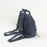 Mochila de diseño acolchado con patrón geométrico en relieve, color azul marino. Cuenta con doble asa superior, bolsillo frontal con cierre, compartimentos laterales y un colgante decorativo de cordón con cuentas de colores en el tirador del cierre.