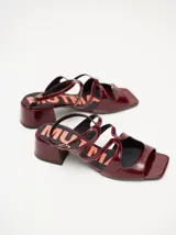 Sandalias de cuero con acabado de charol en color bordó, con diseño de tiras cruzadas, punta cuadrada y taco bloque de 4,5 cm. Incluyen correa ajustable con hebilla en el tobillo.