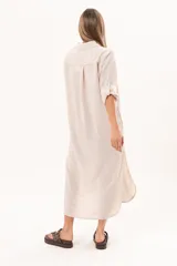 Vestido camisero largo de lino color beige, con silueta relajada, abotonado al frente, cuello camisero, mangas regulables y tajos laterales.