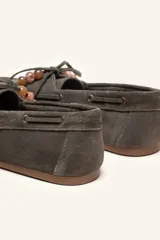 Mocasín estilo náutico de gamuza marrón, con cordones de cuero, borla decorativa y cuentas de colores en el empeine.