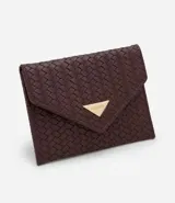 Billetera pequeña tipo sobre con textura trenzada tressê, confeccionada en cuero sintético. Presenta un cierre con botón a presión y un aplique metálico triangular decorativo en la solapa.