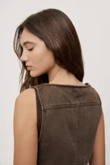 Chaleco corto de denim negro con escote en V y diseño sin mangas. Presenta terminación lavada y detalles laterales con entramado y tachas metálicas que aportan un toque distintivo.