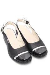 Zapato de cuero negro con talón descubierto, hebilla lateral y punta charolada con aplique plateado.