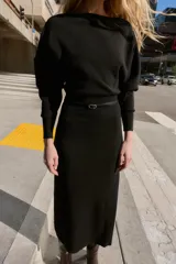Vestido midi de punto en color negro, con cuello barco y mangas largas con sisa ancha. Presenta una cintura entallada con un cinturón fino incorporado con hebilla metálica dorada.