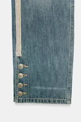 Jeans rectos de tiro medio en denim azul con efecto deslavado. Presentan bandas laterales con detalles brillantes, bolsillos delanteros y traseros, y aberturas en los tobillos con botonadura metálica.