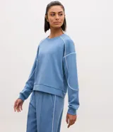 Buzo deportivo Get Over oversized de modal en color celeste, con cuello redondo, manga larga y detalles de costuras y frisos en color blanco.