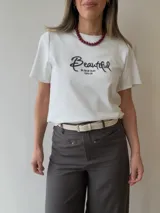 Remera azul marino de manga corta y corte clásico, con estampa bordada con la palabra "Beautiful" en el frente. Incluye un pañuelo de cuello con estampado a cuadros en tonos oscuros.