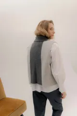 Chaleco abierto de tejido de punto, con diseño de bloques de color verticales en gris claro, negro y gris oscuro. Presenta un cuello ancho tipo chal y un detalle de tres pequeñas aplicaciones bordadas horizontales en tonos verde oliva, naranja quemado y celeste pálido en el frente.