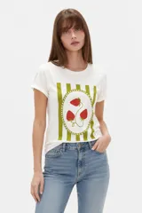 Remera de manga corta blanca con cuello redondo, diseño holgado y estampado frontal de fresas con fondo de rayas verdes.